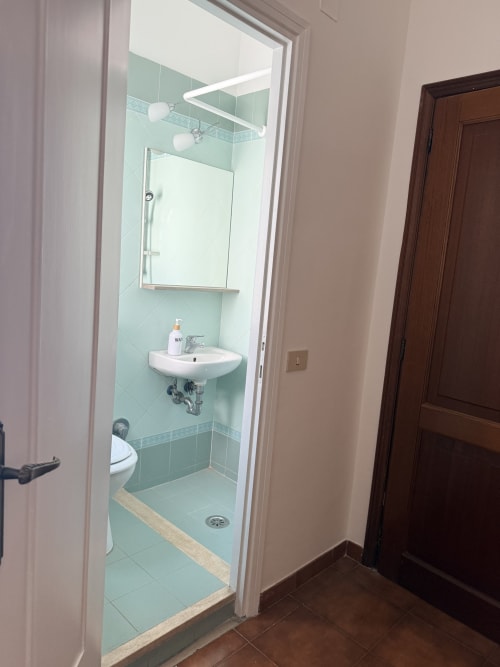 Modern bathroom with light green tiles, white sink, glass shower enclosure, and toilet at Claudia Apartments Rome