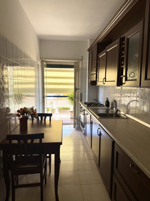 Modern kitchen with dining area in Claudia Apartments Rome, featuring dark cabinets, stainless steel appliances, and balcony