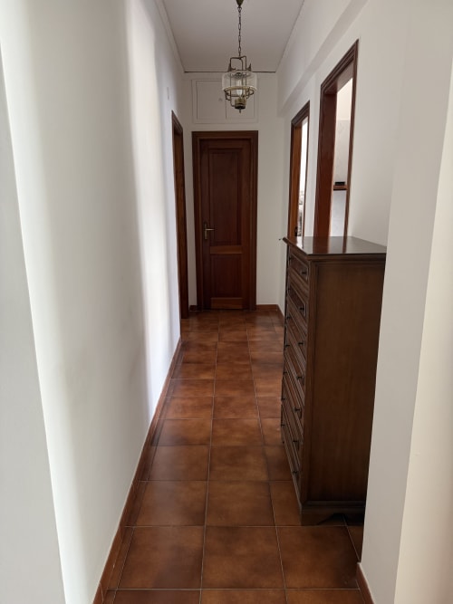 Long hallway in Claudia Apartments Rome with terracotta tile floors, white walls, dark wooden doors, and pendant lighting