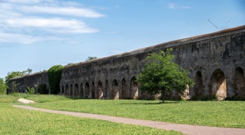 Historic Roman aqueduct ruins with arches in Cinecittà area near Rome Metro, greenery surrounding ancient stone structure