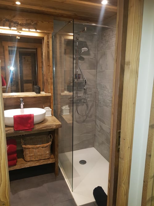 Salle de bains moderne dans un appartement de Courchevel avec douche à l'italienne, vasque blanche, meuble en bois, sèche-serviettes électrique et