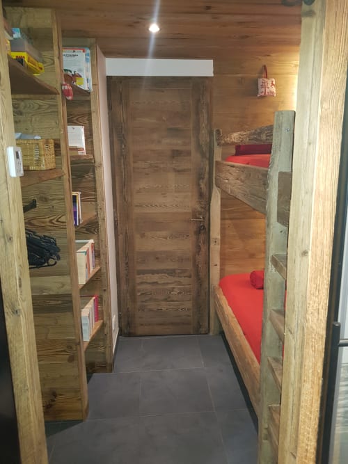 Couloir cosy d'un appartement de ski avec lits superposés en bois, literie rouge, étagères et sol foncé à Courchevel Village