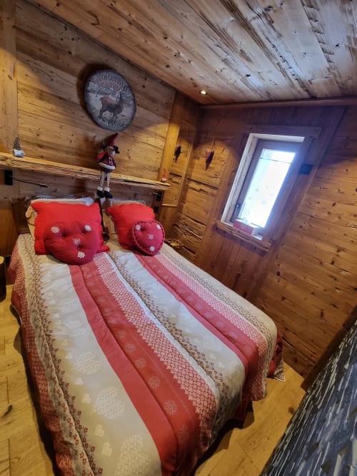 Chambre douillette d'un appartement de ski à Courchevel avec literie rayée rouge, murs en bois, horloge alpine et vue sur les montagnes