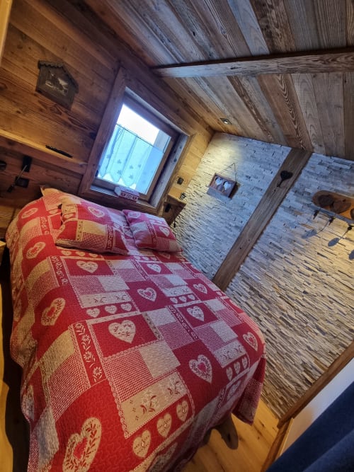 Chambre cosy en bois avec literie à motifs rouges, vue sur fenêtre et poutres apparentes dans un appartement de Courchevel