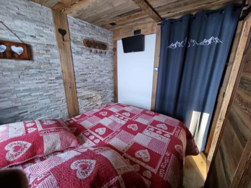 Chambre cosy d'appartement à Courchevel avec literie à motifs rouges, murs en pierre apparente, poutres en bois, TV et vue montagne