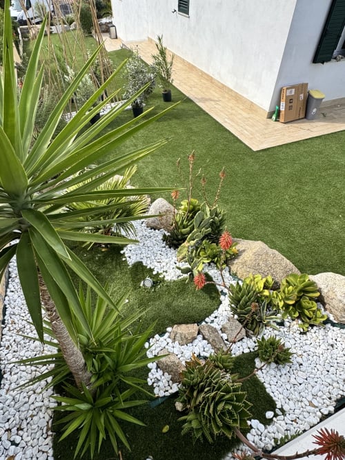 Giardino cortilizio moderno di Villa Carrie Porto Pozzo con piante grasse, ghiaia bianca, prato sintetico verde e legno