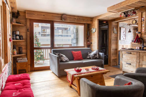 Appartement ski-in ski-out confortable à Courchevel Village avec intérieur en bois, canapé gris, accents rouges, cheminée et vue sur les montagnes