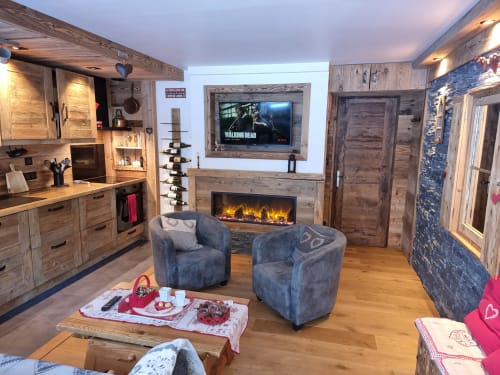 Appartement de ski douillet avec cheminée en pierre, télévision écran plat, fauteuils bleus, cuisine en bois et décor de chalet montagnard