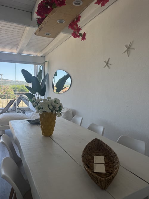 Luminosa zona pranzo dell'Appartamento Starfish a Villa Carrie con vista mare, sedie bianche, fiori in vaso e arredamento costiero