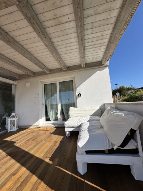Terrazza soleggiata dell'Apartment Starfish, Villa Carrie Porto Pozzo, con deck in legno, lettini bianchi e pergolato in legno