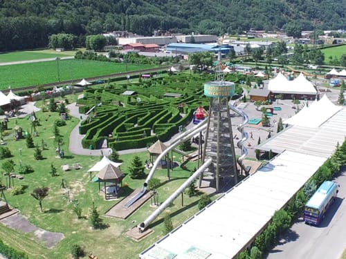 Aerial view of Hôtel Les Triolets in Châtel with maze, playground, and amusement park attractions surrounded by green fields