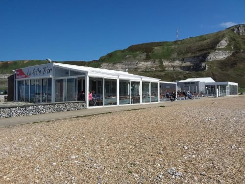 La Petite D'Or beachfront restaurant with white exterior and glass windows on pebble beach near Étretat, France