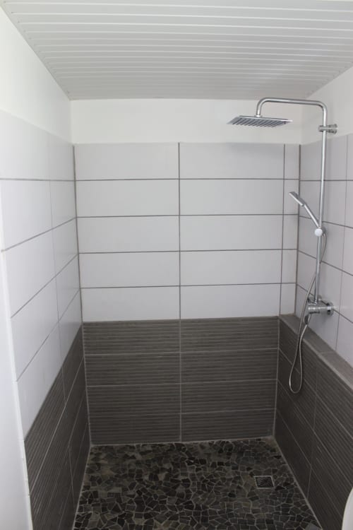 Salle de bain moderne avec carrelage blanc et noir, pomme de douche pluie et sol en galets du bungalow Résidence B&L Lagon
