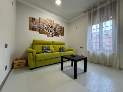 Luminosa sala de estar en Apartamentos RJ26 León con sofá verde lima, mesa negra y obra de arte con árbol