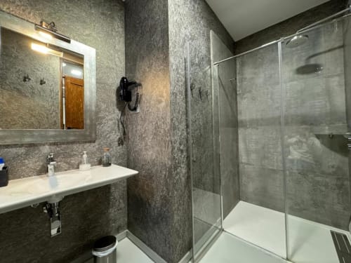 Baño moderno en Apartamentos RJ26 León con azulejos grises, ducha a ras de suelo, lavabo y espejo iluminado