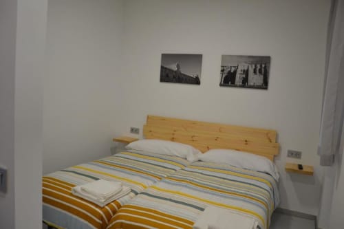 Dormitorio en Apartamentos RJ26 León con cabecero de madera, ropa de cama rayada y fotografías vintage en paredes blancas