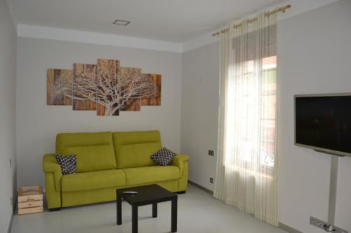 Sala luminosa en Apartamentos RJ26 León con sofá verde lima, televisor de pantalla plana y obra de arte con árbol