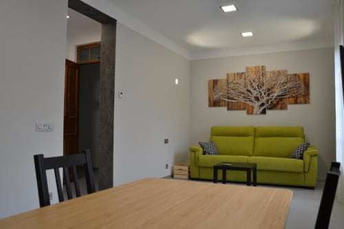 Moderna sala de estar con sofá verde lima, mesa de comedor en madera y arte con árbol en Apartamentos RJ26 León