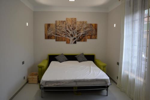 Dormitorio moderno en Apartamentos RJ26 León con cama de marco verde lima, ropa de cama blanca, cuadro artístico de árbol sobre la cama e iluminación natural