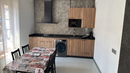 Cocina moderna con muebles de madera, encimera negra, lavadora y mesa de comedor en Apartamentos RJ26 León