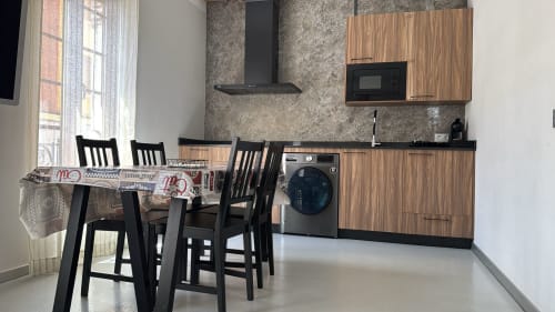 Moderna zona de cocina-comedor en Apartamentos RJ26 León con muebles de madera, sillas negras y lavadora