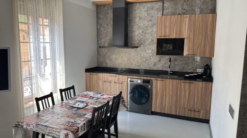 Cocina-comedor moderno en Apartamentos RJ26 León con muebles de madera, encimera negra, mesa de comedor y lavadora