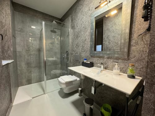 Baño moderno en Apartamentos RJ26 León con azulejos grises, ducha de cristal, tocador blanco y vista a la ciudad