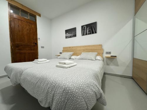 Dormitorio moderno en Apartamentos RJ26 León con cabecera de madera, ropa de cama blanca con patrón y decoración con vista a la ciudad