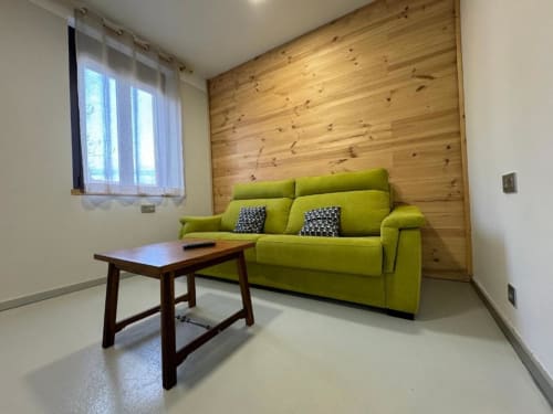 Luminoso salón en Apartamentos RJ26 León con sofá verde lima, pared de madera y vistas a la ciudad