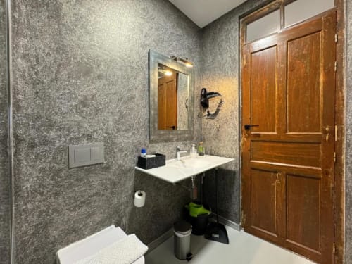 Baño moderno en Apartamentos RJ26 León con paredes de azulejos grises, lavamanos blanco, mueble de madera y vistas a la ciudad