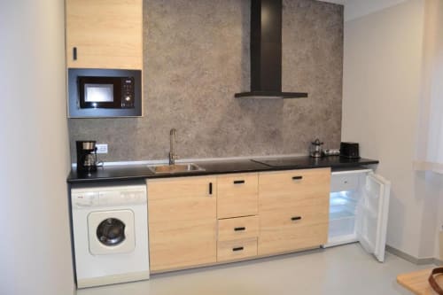 Cocina moderna en Apartamentos RJ26 León con encimera negra, armarios de madera, microondas integrado y acero inoxidable