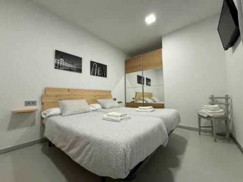 Dormitorio moderno en Apartamentos RJ26 León con cabecera de madera, armario espejado y mobiliario contemporáneo
