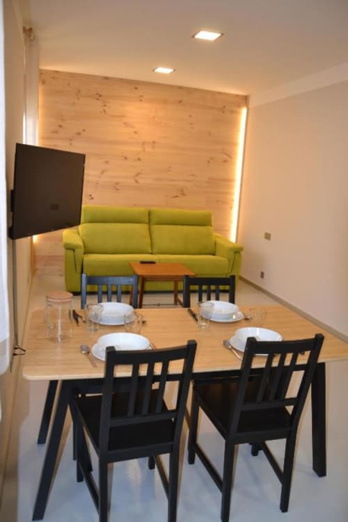 Comedor moderno con mesa de madera, sillas negras, sofá verde lima y pared de acento de madera con iluminación ambiental