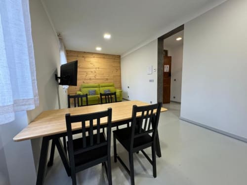 Comedor moderno con mesa de madera, sillas negras, sofá verde y pared de paneles de madera en Apartamentos RJ26