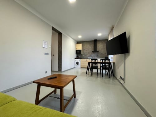 Apartamento moderno en RJ26 León con sala abierta, mesa de madera, cocina, comedor y TV en pared