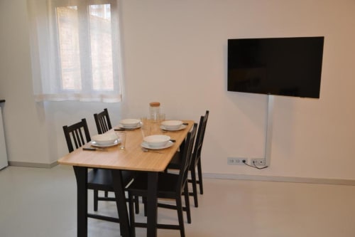 Zona de comedor en Apartamentos RJ26 León con mesa de madera, sillas negras, servicio de mesa y televisor montado en la pared