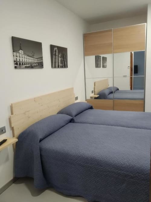 Dormitorio moderno en Apartamentos RJ26 León con cama doble, cabecero de madera clara, ropa de cama azul y armario espejado