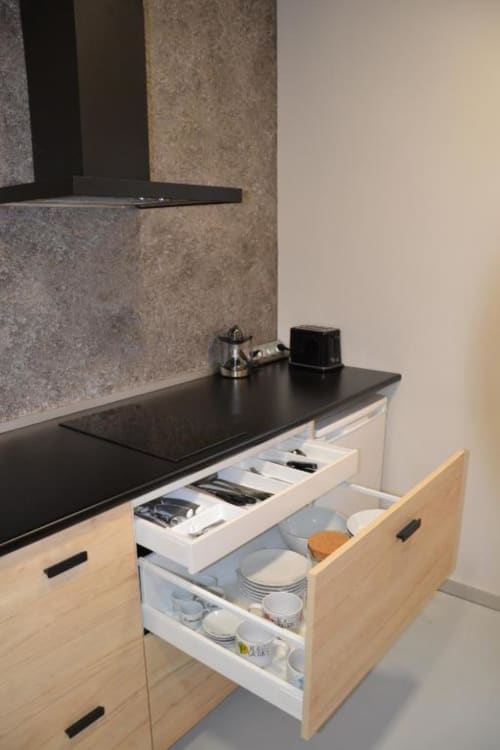 Almacenamiento de cocina moderno con cajones abiertos mostrando loza y utensilios, encimera negra, cabinetería de madera clara