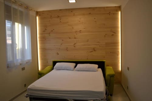 Moderno dormitorio en Apartamentos RJ26 León con pared de madera, iluminación ambiental, ropa de cama blanca y sillones verde lima.