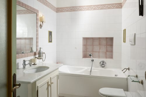 Luxury bathroom at Villa Stecchini Resort with white tiles, pink accents, marble-framed mirror, vanity sink, and soaking tub
