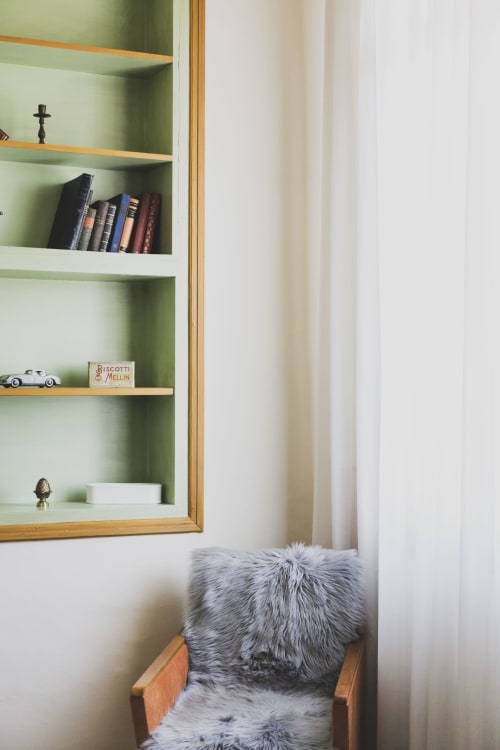 Cozy reading nook at Villa Stecchini Resort with wooden shelving, books, and gray faux fur armchair by window