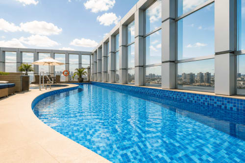 Piscina de luxo na cobertura com vista da cidade em ALUGUEASY em Brasília, com azulejos azuis, espreguiçadeiras e vidro moderno