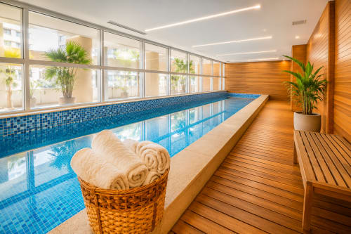 Piscina coberta com azulejos azuis, deck de madeira e vista da cidade no hotel ALUGUEASY Brasília