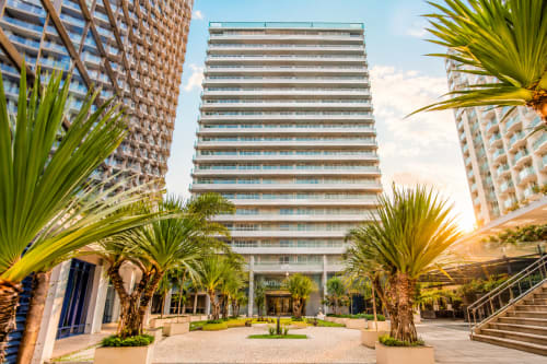 Pátio de hotel moderno em Brasília com palmeiras, edifícios residenciais e arquitetura contemporânea sob céu limpo