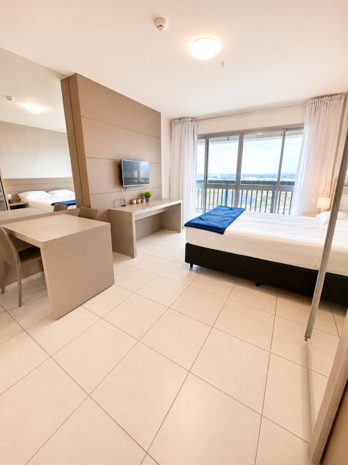 Quarto de hotel moderno em Brasília com cama, escrivaninha, varanda com vista da cidade e design acessível para cadeira de rodas