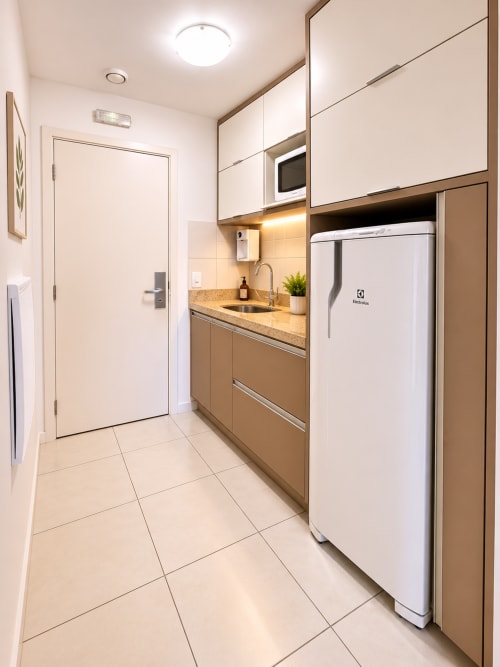 Cozinha moderna em Brasília BnB com armários brancos, bancada em granito, geladeira Electrolux branca e piso em azulejo bege