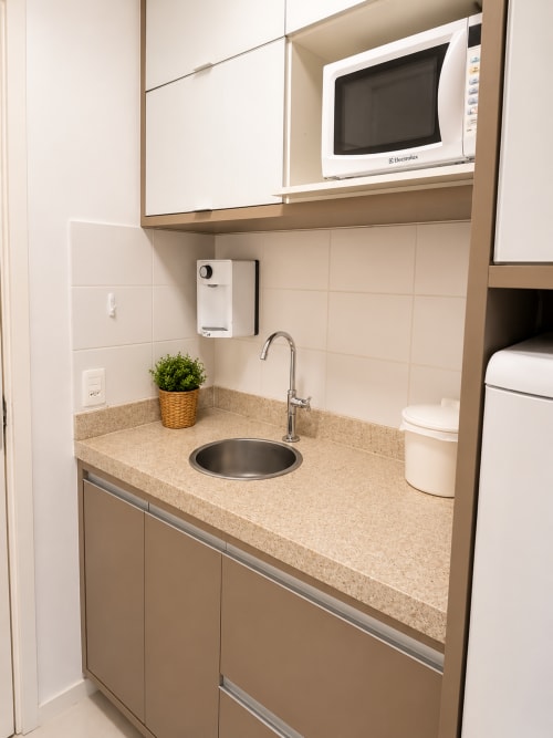 Kitchenette compacta com pia, micro-ondas, bancada bege e azulejo branco na sala da Pousada em Brasília