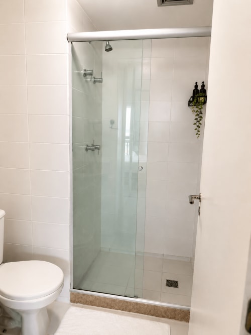 Banheiro moderno com box de vidro, azulejos brancos, vaso sanitário e prateleira de amenities em quarto de hotel em Brasília
