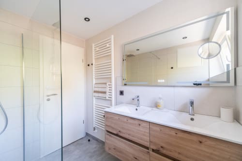 Baño moderno en apartamento Les Ambrades con doble tocador, espejo grande, ducha walk-in y mobiliario de madera
