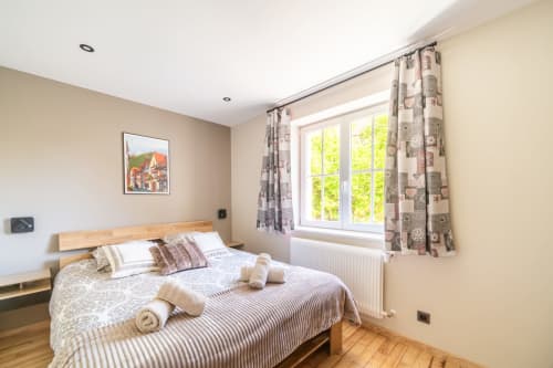 Dormitorio luminoso en Les Ambrades, Kaysersberg con cama queen, cortinas estampadas, amplias ventanas con vistas al pueblo, y madera